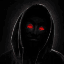 a man in a hooded sweatshirt with red eyes is standing in the dark .