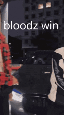 a man in a red plaid shirt is standing in front of a car with the words bloodz win written on the screen