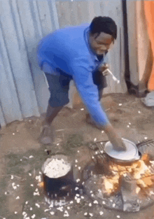 a man in a blue shirt is cooking food on a stove outside .