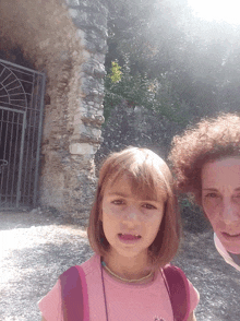 a little girl in a pink shirt stands next to a woman in a red shirt