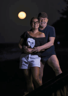 a man and a woman are posing for a picture with the moon in the background