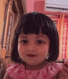 a little girl with short black hair is wearing a pink dress and necklace .