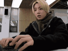 a man with blonde hair is typing on a laptop computer .