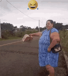 a woman in a blue dress is standing on the side of a road with a smiley face flying in the air behind her .