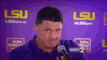 a man in a blue shirt is talking into a microphone in front of a purple background .