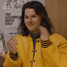 a young man wearing a yellow jacket is smiling in front of a poster that says the wonderful crowd band