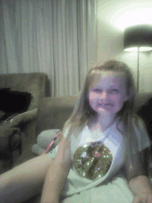 a little girl is sitting on a couch wearing a shirt with a donut on the front