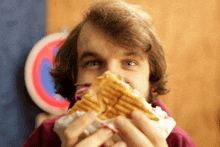 a man is eating a sandwich with a no parking sign in the background