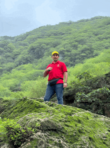 a man in a red shirt and yellow hat stands on a rock