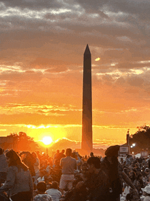 a crowd of people are gathered in front of a washington monument at sunset