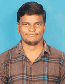 a man in a plaid shirt is standing in front of a blue background and looking at the camera .