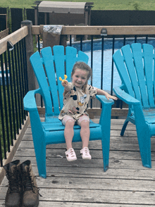 a little girl is sitting in a blue chair on a deck