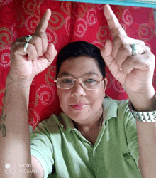 a man wearing glasses and a green shirt is giving a peace sign