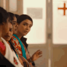 a group of women are sitting in a row in front of a window with a red cross on it .