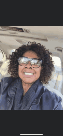 a woman with curly hair wearing sunglasses and a jacket smiles for the camera