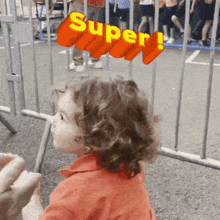 a little girl with curly hair is standing in front of a fence with the word super above her head