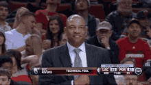 a man in a suit and tie stands in front of a crowd at a basketball game with technical foul written on the screen