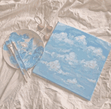 a painting of clouds on a canvas next to a plate of paint