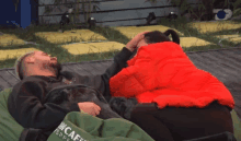 a man and a woman are laying on a bean bag chair and the woman is wearing a red jacket