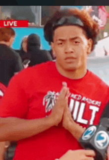 a man wearing a red shirt with the word ult on it is praying