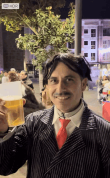 a man in a suit and tie holds a glass of beer in front of a hdr sign