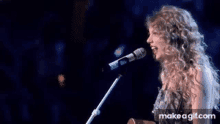 taylor swift is singing into a microphone while holding a guitar on stage .