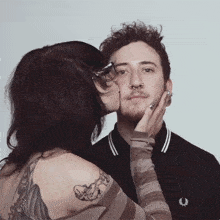 a woman is kissing a man on the cheek who is wearing a black shirt with a laurel wreath on it