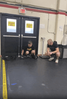 a man squatting on the floor in front of a sign that says exit