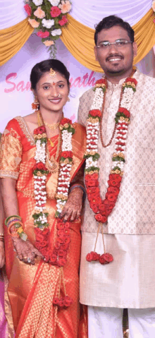 a man and a woman are posing for a picture in front of a sign that says ' sampath '