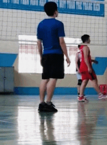 a man in a blue shirt and black shorts stands on a basketball court in front of a banner that says " boy team "