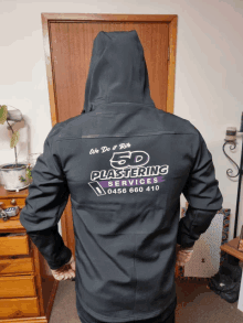 a person wearing a black jacket with 5d plastering services written on the back