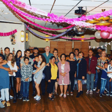 a large group of people posing for a picture in a room decorated with pink paper streamers