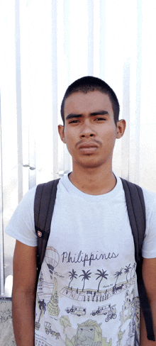 a man wearing a philippines t-shirt stands in front of a white wall