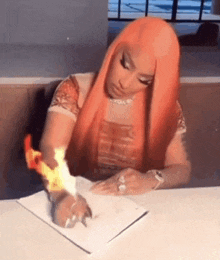 a woman with long red hair is sitting at a table holding a piece of paper with flames coming out of it .