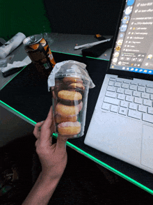 a person holding a cup of donuts next to a laptop