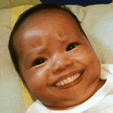 a baby is smiling and making a funny face while laying on a blanket .