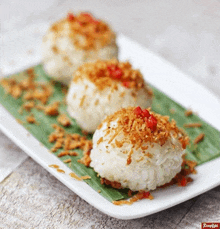 a white plate topped with three rice balls with a red pepper on top .