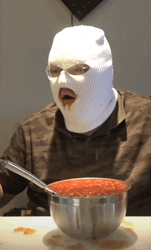 a man wearing a ski mask is eating a bowl of sauce