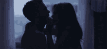 a man and woman are kissing in front of a window in the dark .