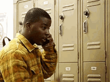 a man in a plaid shirt is talking on a cell phone in front of a row of lockers .