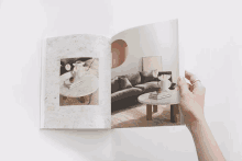 a person is holding a book with a picture of a couch and a table