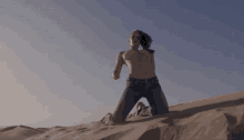 a naked woman is kneeling on a sand dune .