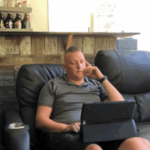 a man sitting on a couch using a tablet with a bottle of maple syrup on the shelf behind him