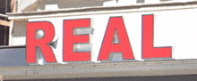 the word real is written in red on a white sign