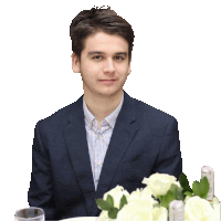 a man in a suit is sitting at a table with flowers in front of him