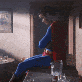 a man in a superman costume sits at a table with a pitcher of beer
