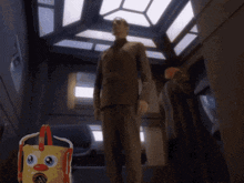 a man in a suit stands in a hallway next to a toy bucket