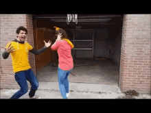 a man in a yellow shirt and a woman in a red shirt are dancing in front of a garage door .