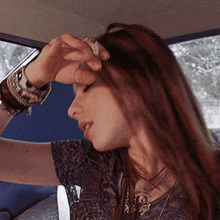 a woman with long hair is sitting in a car holding her hand to her forehead