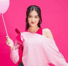 a girl in a pink sweater is holding a pink balloon .